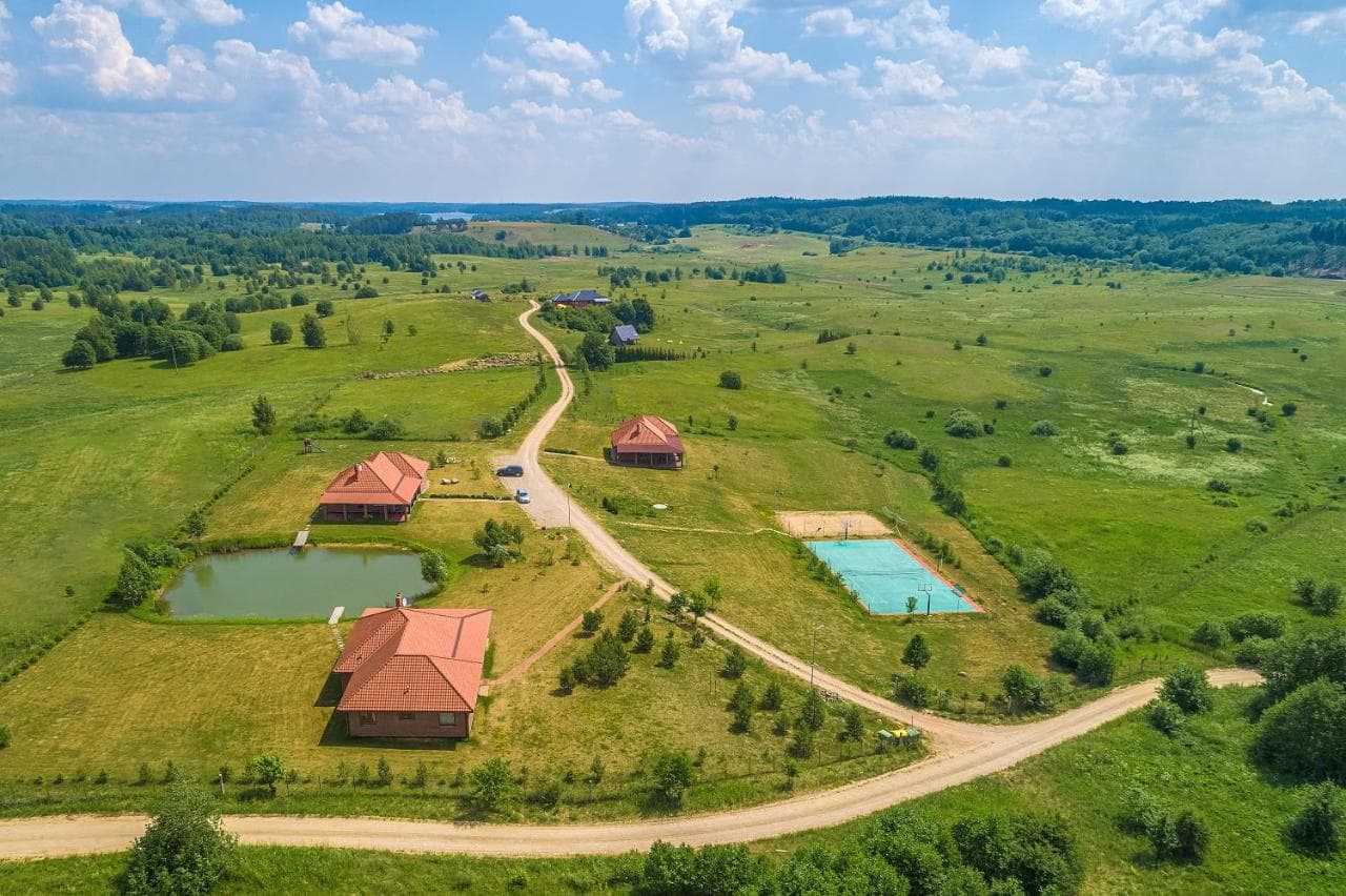 Sodybos vaizdas iš paukščio skrydžio — keli svečių namai, tvenkinys ir teniso aikštelė
